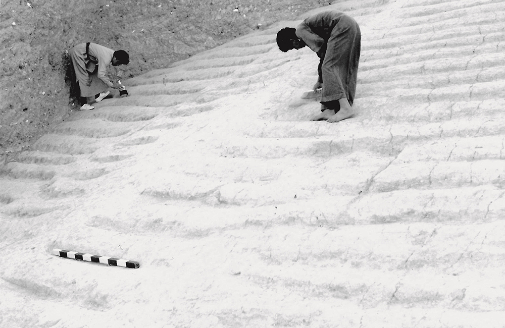 Two people in long robes bent over working on the White Monument